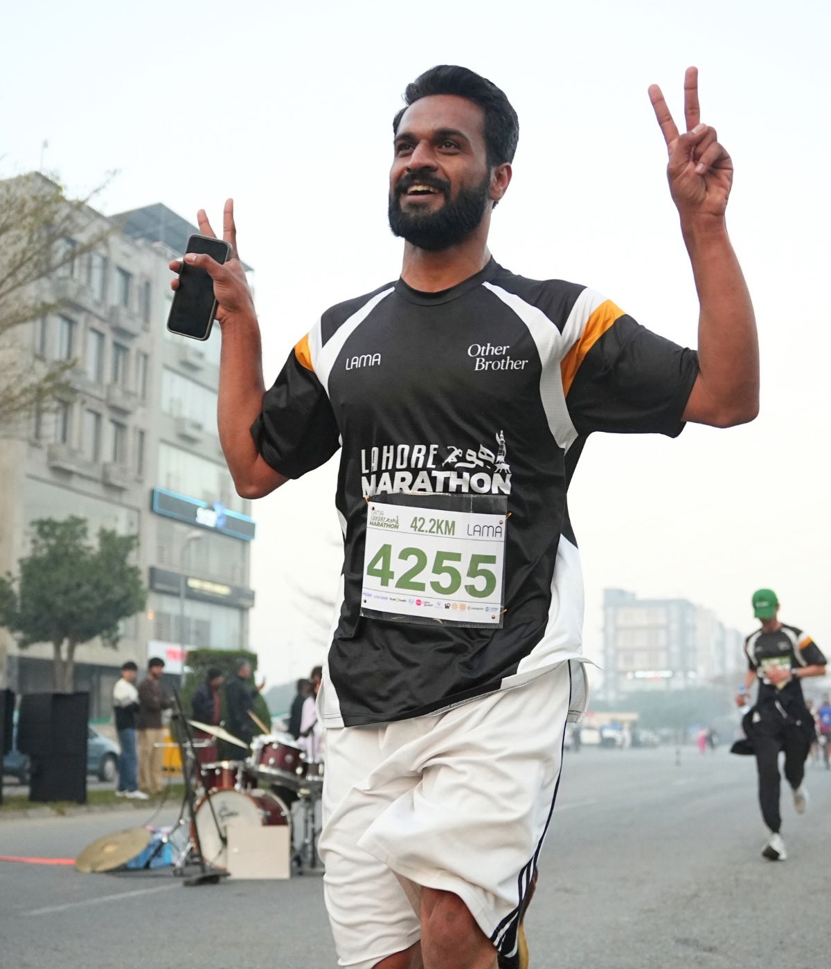 A Lahore Marathon runner in a race vest, bib 4255 visible, making a peace sign