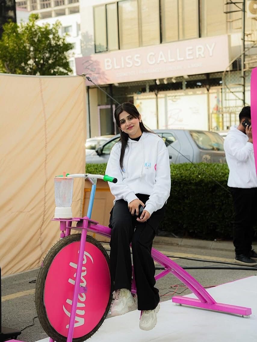 A woman seated on a pink smoothie bike at a Marathon Village stall